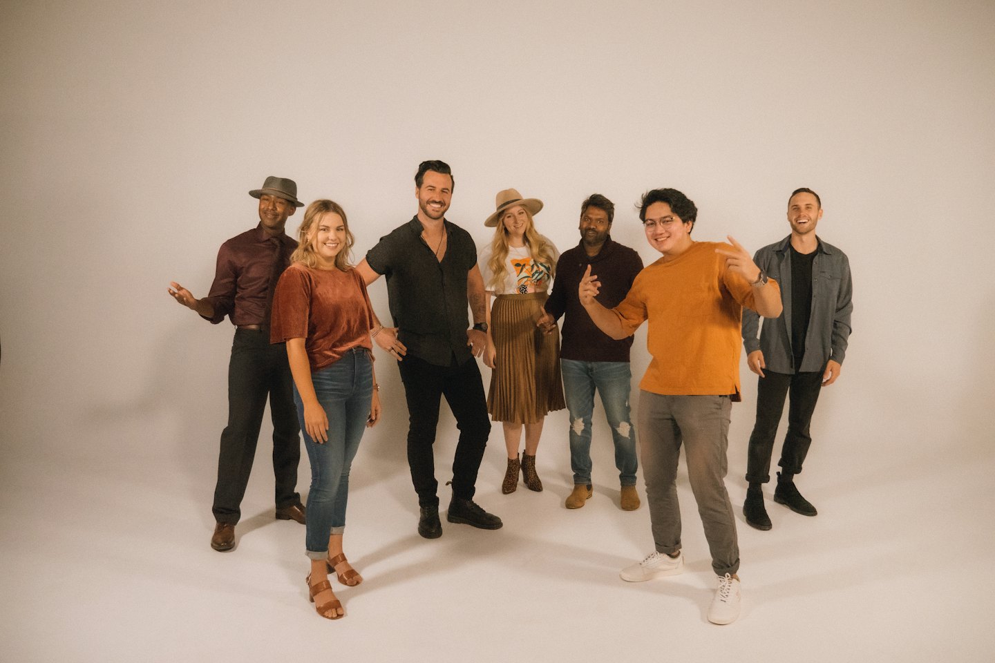 Six people stand together smiling against a white wall.